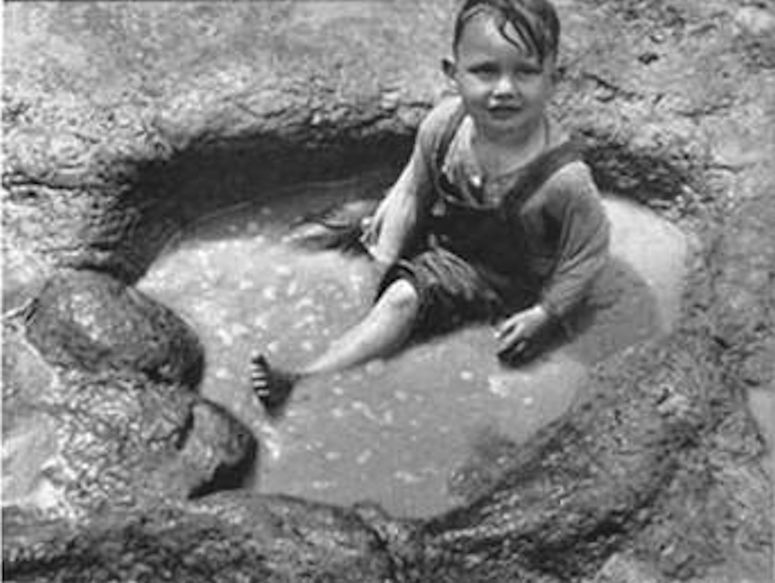 A child taking a bath in a dinosaur fossil footprint.